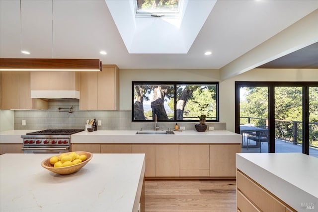 kitchen with sink, a skylight, stainless steel range, light brown cabinetry, and decorative backsplash