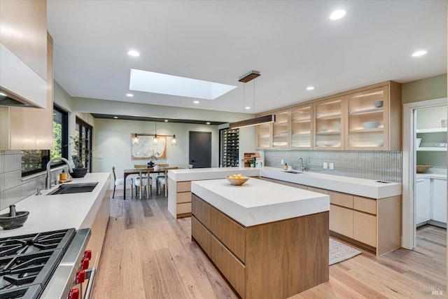 kitchen featuring pendant lighting, a skylight, sink, light hardwood / wood-style floors, and a spacious island