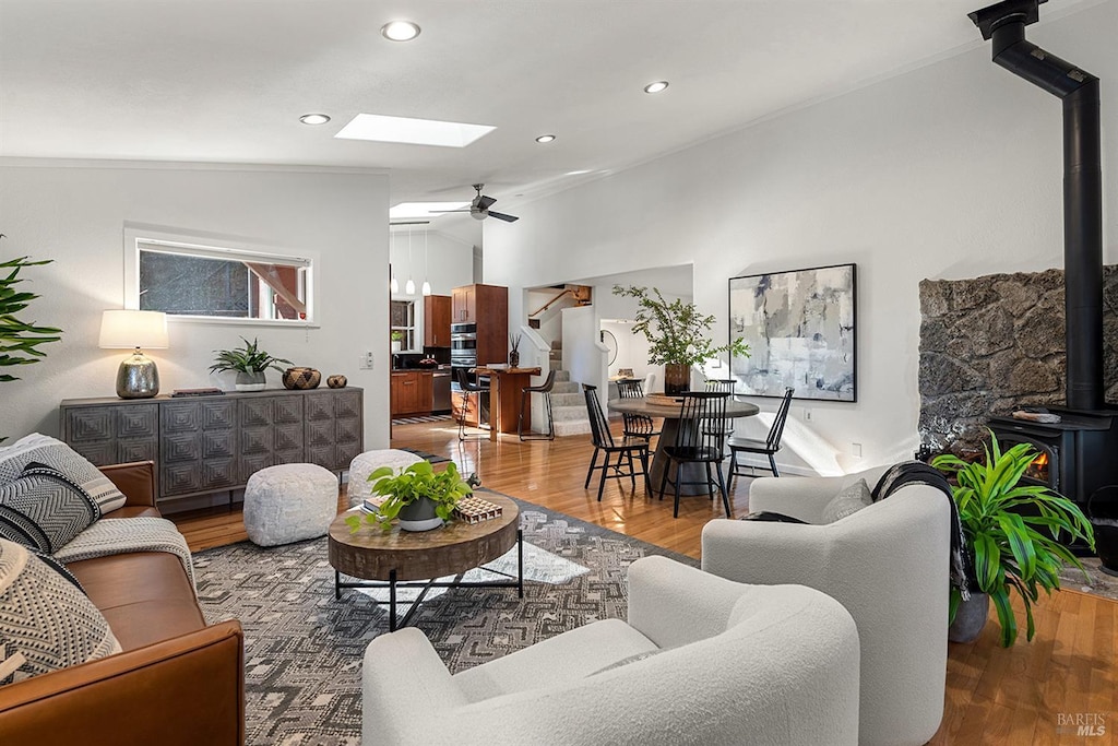 living room with ceiling fan, lofted ceiling with skylight, hardwood / wood-style floors, and a wood stove