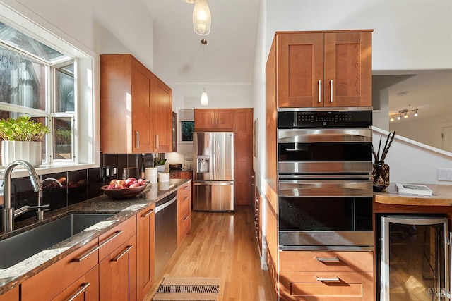 kitchen featuring wine cooler, sink, stone countertops, light hardwood / wood-style flooring, and appliances with stainless steel finishes