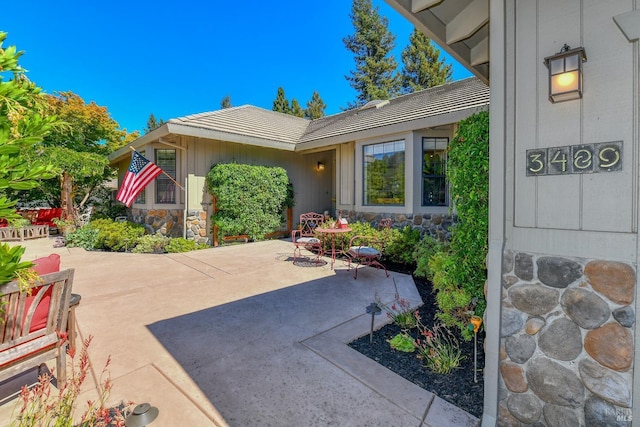 entrance to property featuring stone siding, a tile roof, and a patio area