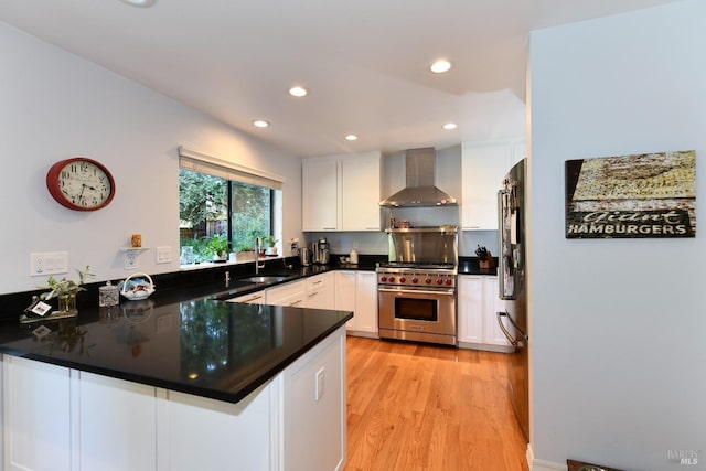 kitchen featuring a sink, white cabinetry, a peninsula, premium range, and wall chimney range hood