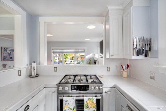 kitchen featuring gas range, backsplash, tile countertops, and white cabinets