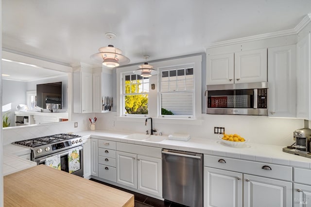 kitchen featuring sink, tile countertops, ornamental molding, stainless steel appliances, and white cabinets