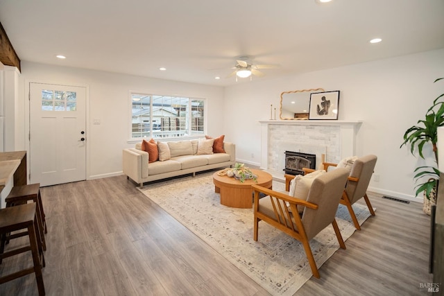 living room featuring hardwood / wood-style flooring, ceiling fan, and a brick fireplace