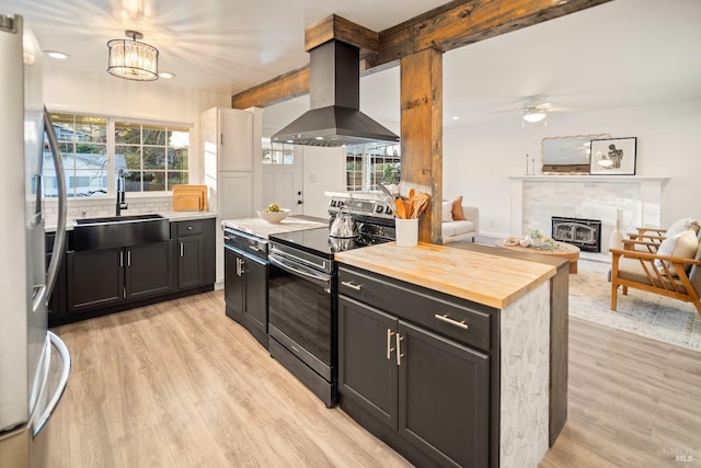 kitchen with appliances with stainless steel finishes, wood counters, sink, island exhaust hood, and light hardwood / wood-style flooring