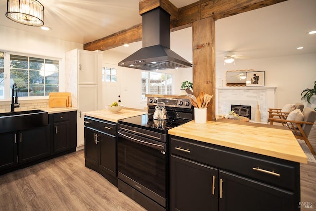 kitchen featuring sink, butcher block counters, island exhaust hood, stainless steel range with electric cooktop, and light wood-type flooring