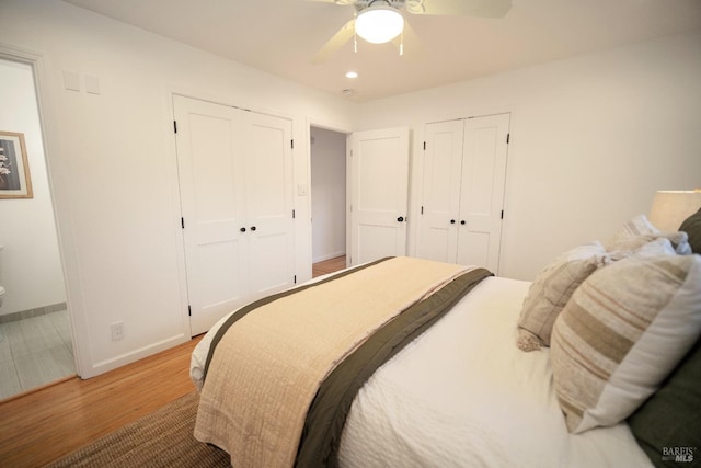 bedroom with two closets, wood-type flooring, and ceiling fan