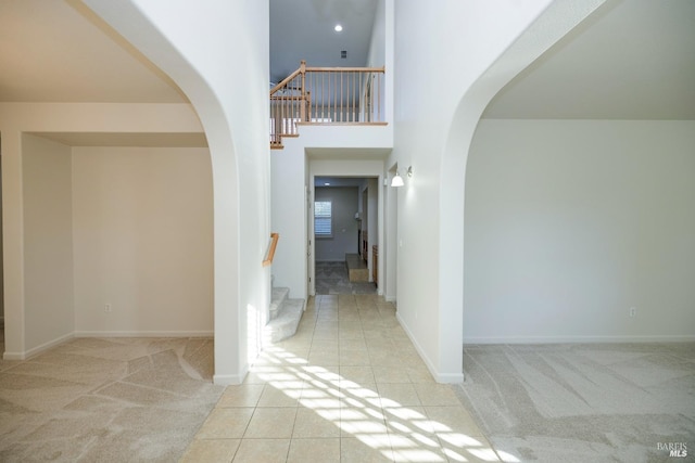 foyer entrance featuring a high ceiling, stairs, arched walkways, and carpet flooring