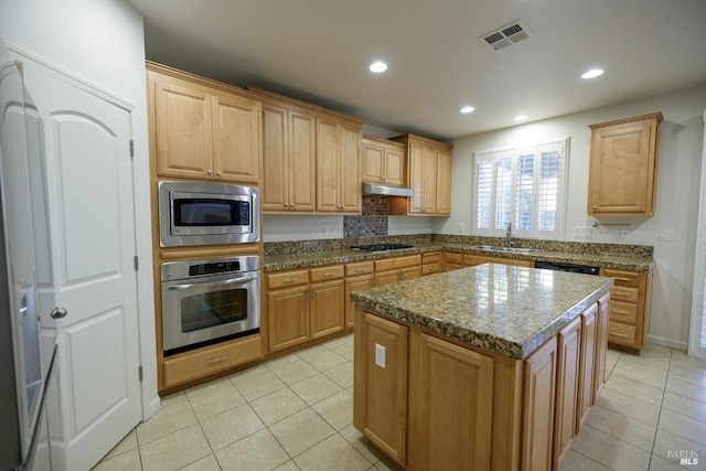 kitchen with sink, light tile patterned floors, appliances with stainless steel finishes, dark stone countertops, and a center island