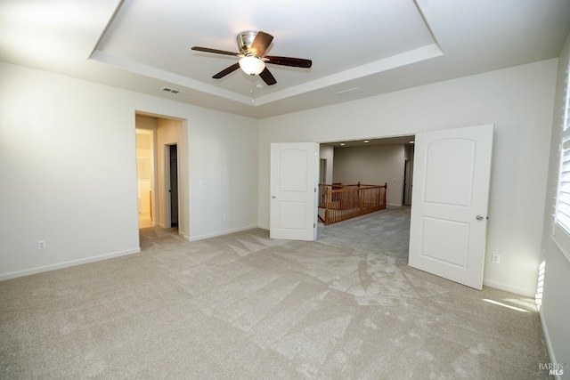 unfurnished bedroom featuring connected bathroom, light colored carpet, ceiling fan, and a tray ceiling