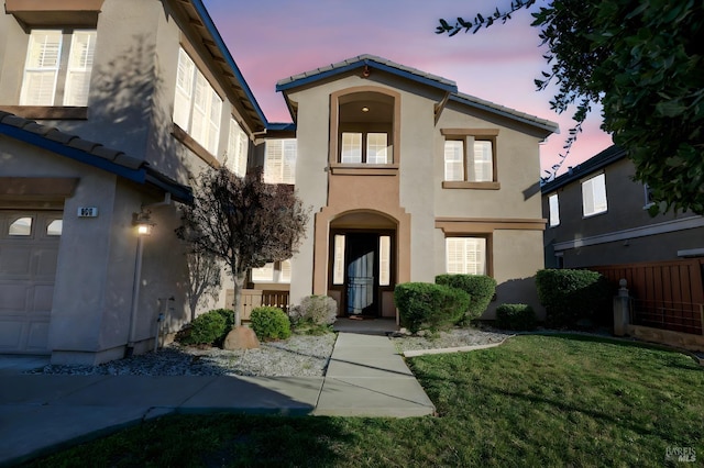 mediterranean / spanish house with a garage, a front yard, a tiled roof, and stucco siding