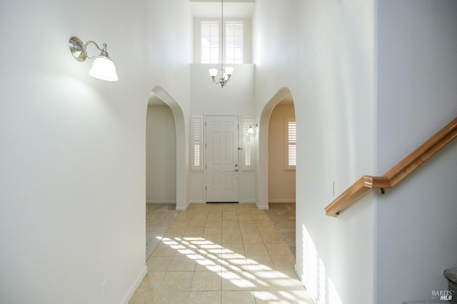 tiled foyer entrance featuring a notable chandelier, a wealth of natural light, and a high ceiling