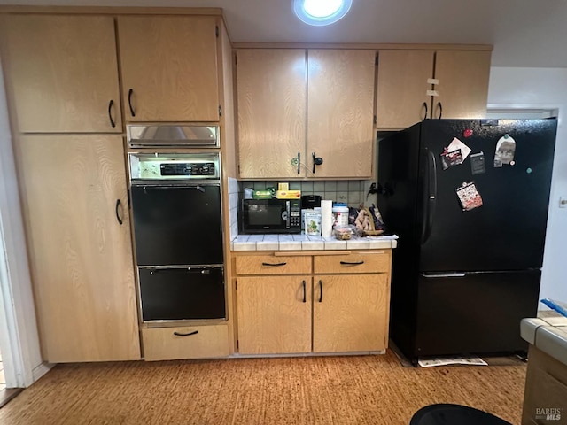 kitchen featuring tile countertops, backsplash, light brown cabinetry, and black appliances