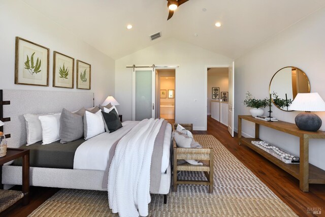 bedroom featuring dark hardwood / wood-style floors, lofted ceiling, ensuite bathroom, and a barn door