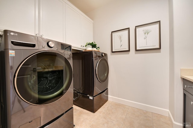 clothes washing area with cabinets, light tile patterned flooring, and washing machine and clothes dryer