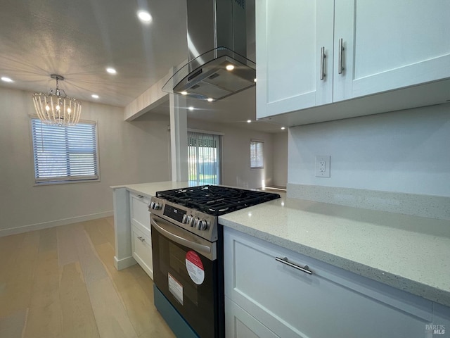 kitchen featuring pendant lighting, stainless steel gas range, light stone countertops, white cabinets, and island exhaust hood