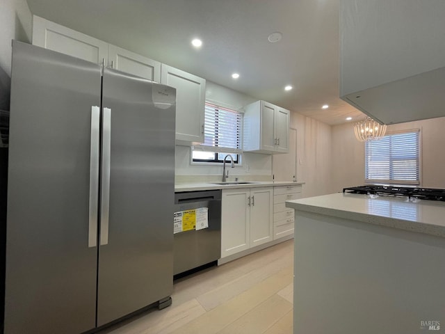 kitchen featuring white cabinetry, light hardwood / wood-style flooring, decorative light fixtures, sink, and appliances with stainless steel finishes