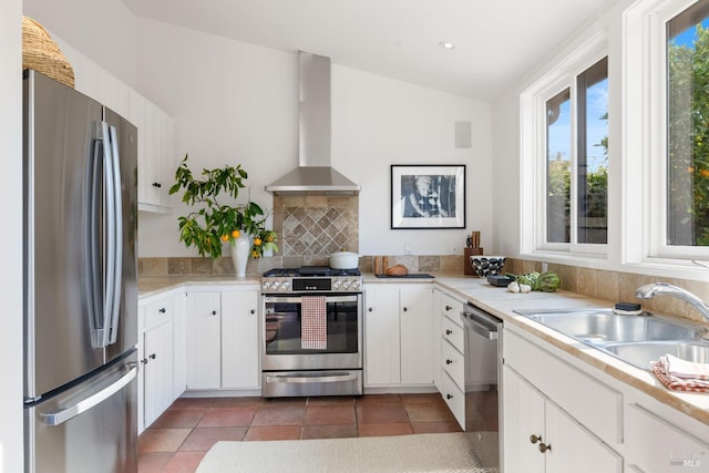 kitchen with vaulted ceiling, appliances with stainless steel finishes, white cabinetry, sink, and wall chimney range hood