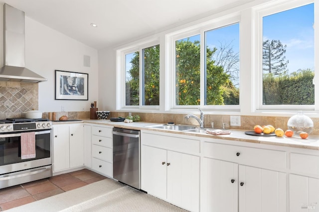 kitchen featuring appliances with stainless steel finishes, white cabinetry, sink, backsplash, and wall chimney exhaust hood