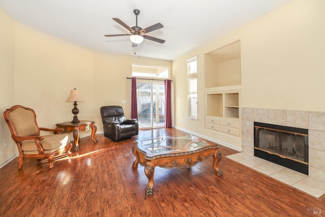 living room featuring a tiled fireplace, built in shelves, light hardwood / wood-style flooring, and ceiling fan