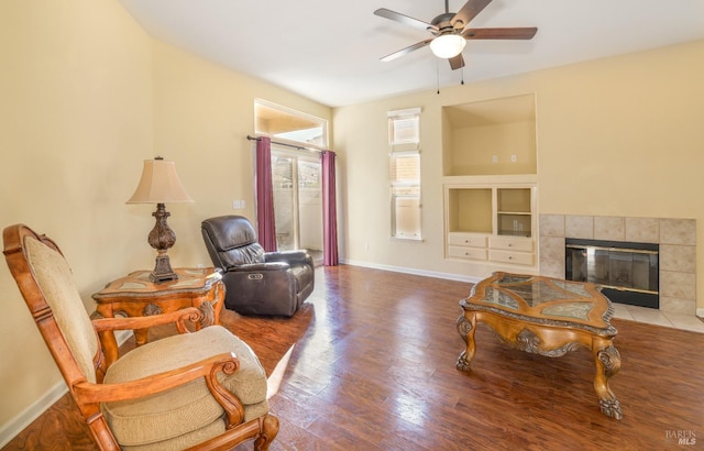 living room with a tiled fireplace, hardwood / wood-style floors, built in features, and ceiling fan