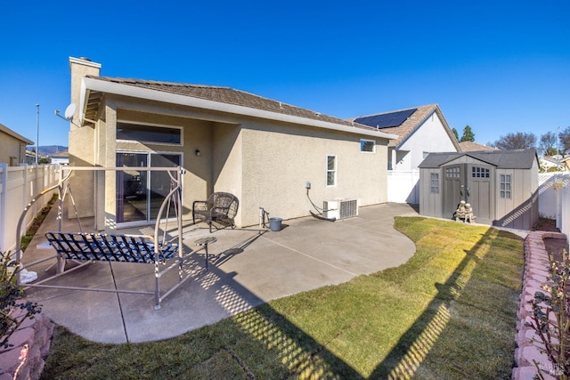 back of house with cooling unit, a storage shed, a yard, and a patio