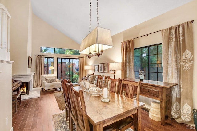 dining space with a notable chandelier, a brick fireplace, hardwood / wood-style flooring, and high vaulted ceiling