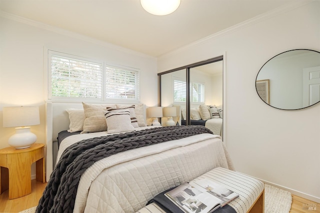 bedroom with light wood-style floors, baseboards, ornamental molding, and a closet