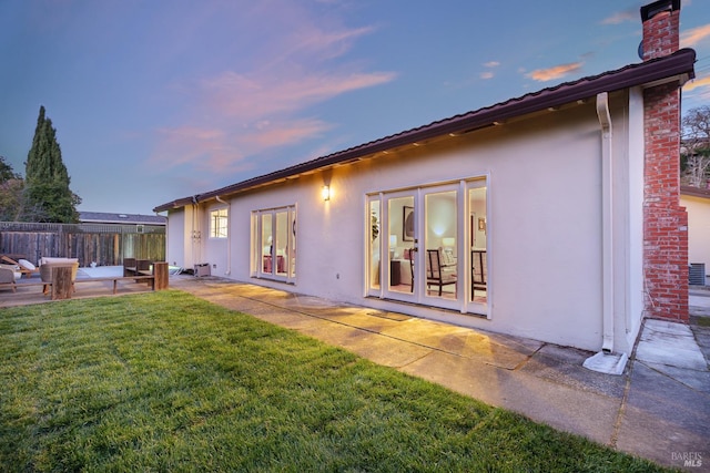 back of house with a chimney, fence, a yard, a patio area, and stucco siding