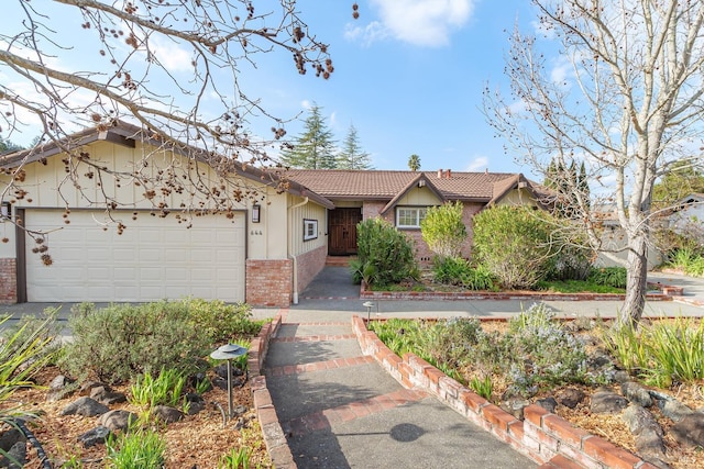 single story home with a garage, driveway, a tiled roof, and brick siding