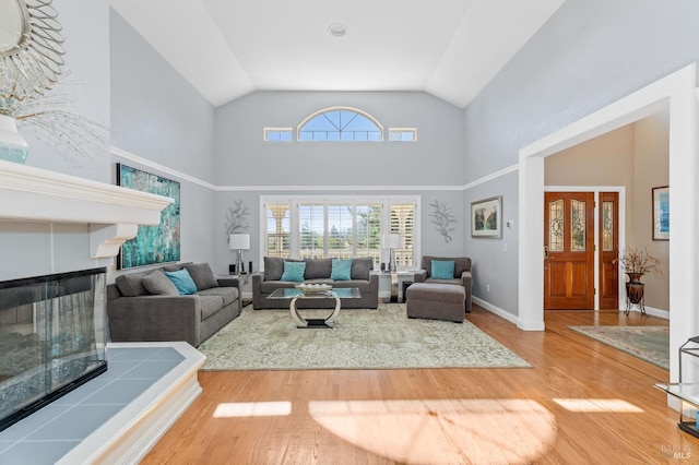 living room featuring hardwood / wood-style flooring, a tiled fireplace, and high vaulted ceiling