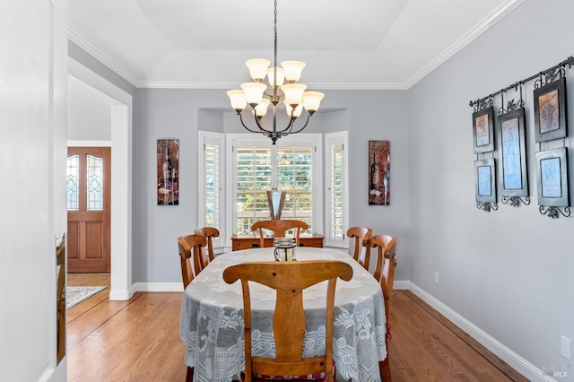 dining room with crown molding, a tray ceiling, a chandelier, and light wood-type flooring