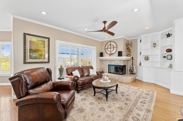 living room featuring crown molding, a fireplace, ceiling fan, and light wood-type flooring