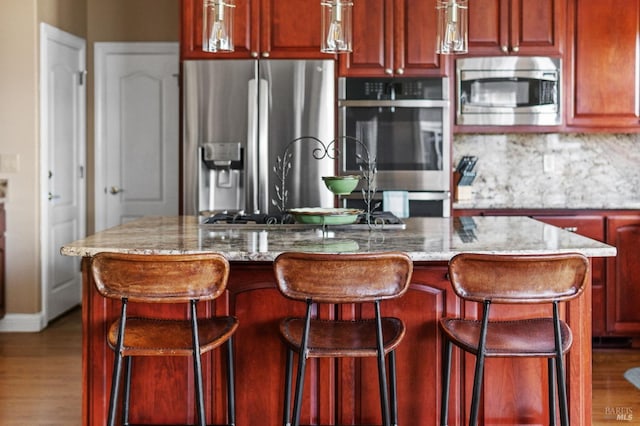 kitchen with appliances with stainless steel finishes, a center island, a breakfast bar area, and light stone counters