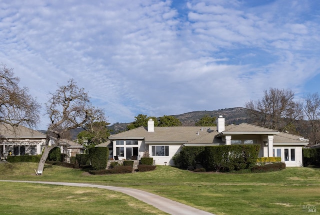 view of front of house featuring a front lawn, a chimney, and a mountain view