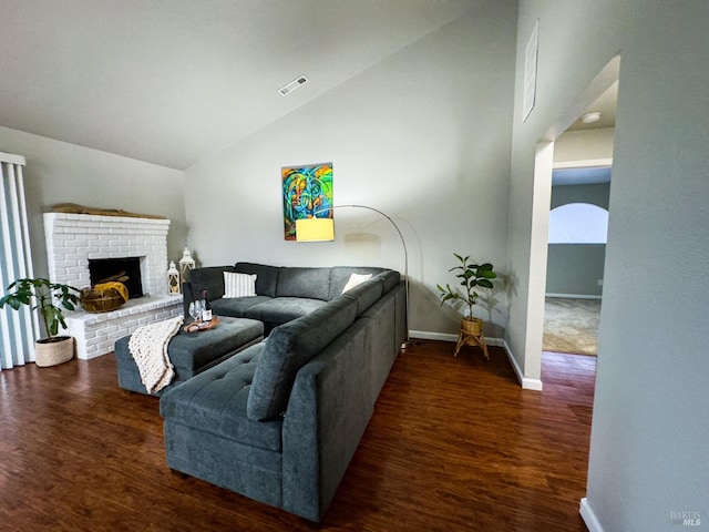 living room with a brick fireplace, visible vents, baseboards, and wood finished floors