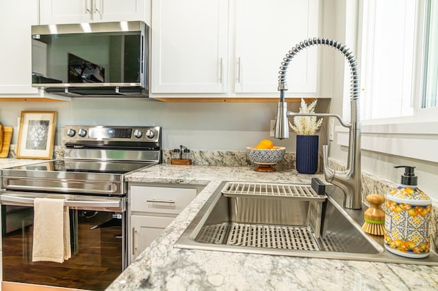 kitchen featuring light stone countertops, white cabinetry, appliances with stainless steel finishes, and a sink