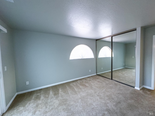 unfurnished bedroom with a closet, carpet flooring, a textured ceiling, and baseboards