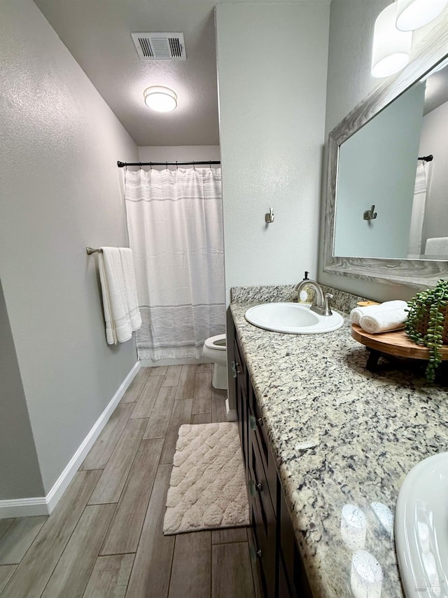 bathroom featuring wood finish floors, visible vents, toilet, vanity, and baseboards