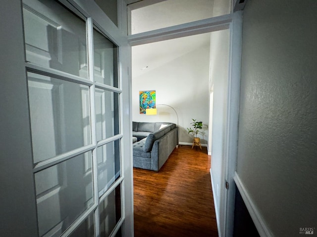 hallway with lofted ceiling, baseboards, wood finished floors, and a textured wall