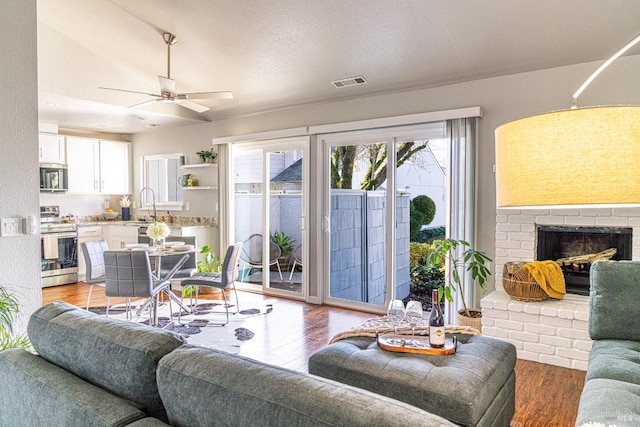 living room featuring ceiling fan, light wood-style flooring, a fireplace, and visible vents