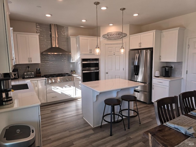 kitchen with hanging light fixtures, stainless steel appliances, a center island, white cabinets, and wall chimney exhaust hood