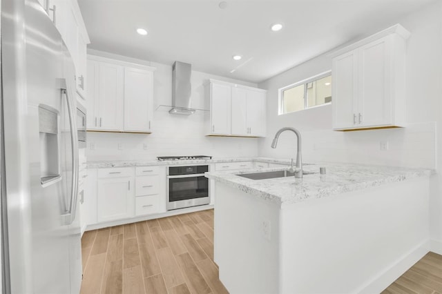 kitchen featuring sink, stainless steel appliances, white cabinets, kitchen peninsula, and wall chimney exhaust hood