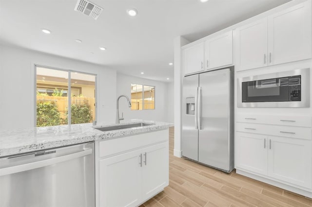 kitchen with sink, stainless steel appliances, white cabinets, and light stone countertops