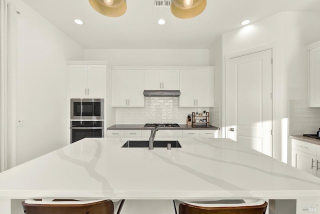 kitchen with tasteful backsplash, appliances with stainless steel finishes, a kitchen island with sink, and white cabinets