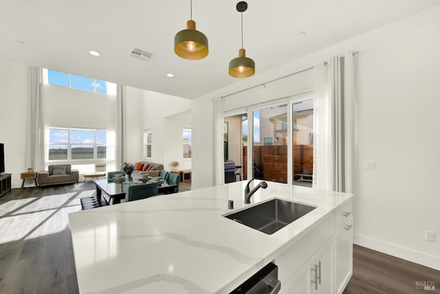 kitchen featuring white cabinetry, sink, dark hardwood / wood-style flooring, hanging light fixtures, and light stone counters