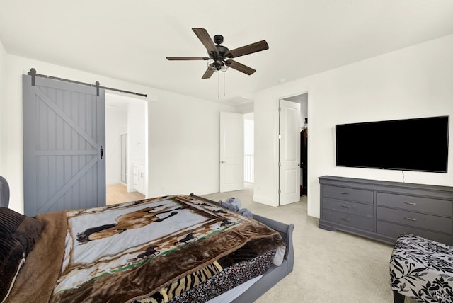 carpeted bedroom with a barn door, connected bathroom, and ceiling fan