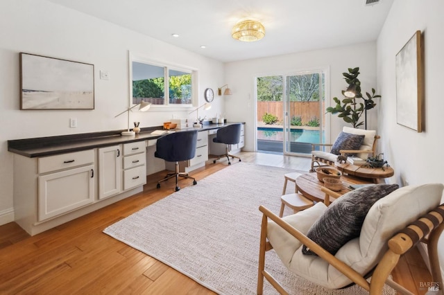 home office with built in desk and light hardwood / wood-style floors