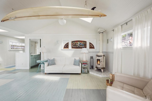 living room with a wood stove, vaulted ceiling with skylight, and light hardwood / wood-style floors